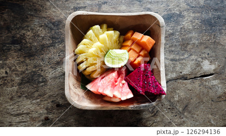 Colorful Assorted Tropical Fruits in Wooden Bowl on Rustic Table Background Offering Fresh Pineapple Watermelon Dragon Fruit and Papaya Slices with a Slice of Lime Colorful Assorted Tropical Fruits in Wooden Bowl on Rustic Table Background Offering Fresh Pineapple Watermelon Dragon Fruit and Papaya Slices with a Slice of Lime 126294136
