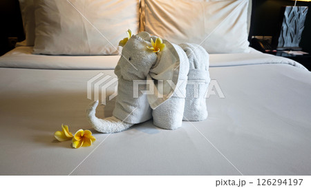 Elegant Elephant-Shaped Towel Art on a Neatly Made Hotel Bed with Frangipani Flowers in a Relaxing Tropical Resort Room Elegant Elephant-Shaped Towel Art on a Neatly Made Hotel Bed with Frangipani Flowers in a Relaxing Tropical Resort Room 126294197