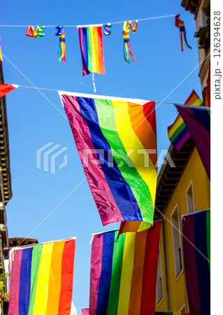 Colorful rainbow flags are strung across a street against a blue sky, decorating city street, celebrating the pride and diversity of lgbtq community. 126294628