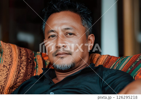 Confident Bhutanese mature male relaxing on patterned couch in casual attire. 126295218