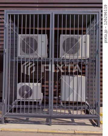 Air conditioning units secured in a metal cage outside a modern building in daytime 126296119
