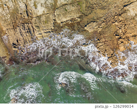Aerial top down view of ocean waves crashing into rocky shore Aerial top down view of ocean waves crashing into rocky shore 126299014