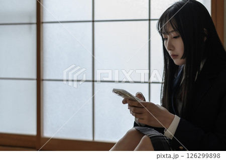 和室内でスマホを見る女子高生　いじめ　不登校　SNSトラブル　トリミングアップ 126299898
