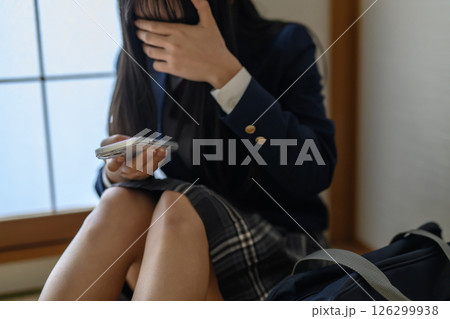 和室内でスマホを見る女子高生　いじめ　不登校　SNSトラブル　朝カラー 126299938