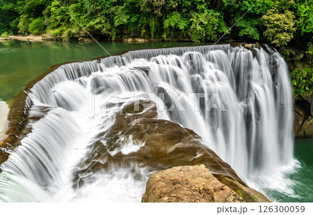 Shifen Waterfall in Pingxi District of New Taipei, Taiwan, cascades powerfully into a turquoise pool amid dense green foliage, offering a scenic and tranquil natural attraction often called the Little Shifen Waterfall in Pingxi District of New Taipei, Taiwan, cascades powerfully into a turquoise pool amid dense green foliage, offering a scenic and tranquil natural attraction often called the Little 126300059