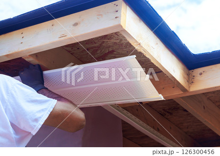 Contractor applies ventilation roof flashing panels to enhance airflow under roof structure at building site. 126300456