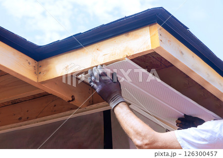 Skilled worker places plastic soffit material in eaves of house while working outdoors. 126300457