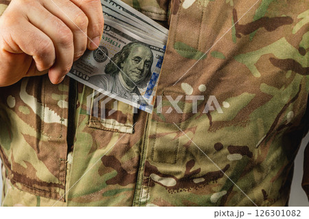 Soldier discreetly tucking money into camouflage pocket Soldier discreetly tucking money into camouflage pocket 126301082