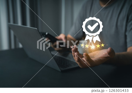 Close-up businessman hand Using Laptop and Smartphone Symbolizing Digital Achievement with Stars, Checkmark, and Award Icon Representing Success and Quality Assurance 126301433