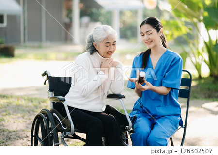 Elderly asian senior woman on wheelchair with Asian careful caregiver and encourage patient, walking in garden. with care from a caregiver. and senior health insurance 126302507