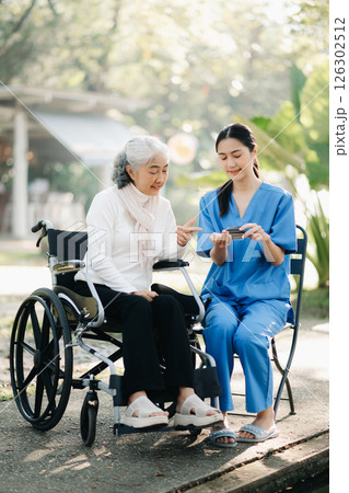 Elderly asian senior woman on wheelchair with Asian careful caregiver and encourage patient, walking in garden. with care from a caregiver. and senior health insurance 126302512
