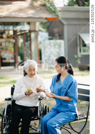 Elderly asian senior woman on wheelchair with Asian careful caregiver and encourage patient, walking in garden. with care from a caregiver. and senior health insurance Elderly asian senior woman on wheelchair with Asian careful caregiver and encourage patient, walking in garden. with care from a caregiver. and senior health insurance 126302526