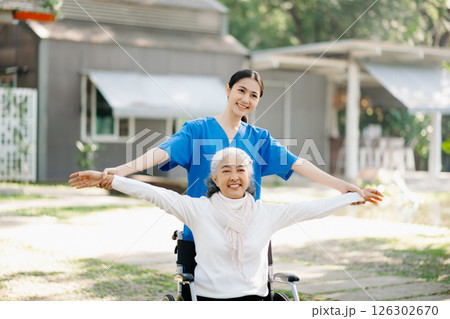 Elderly asian senior woman on wheelchair with Asian careful caregiver and encourage patient, walking in garden. with care from a caregiver Elderly asian senior woman on wheelchair with Asian careful caregiver and encourage patient, walking in garden. with care from a caregiver 126302670