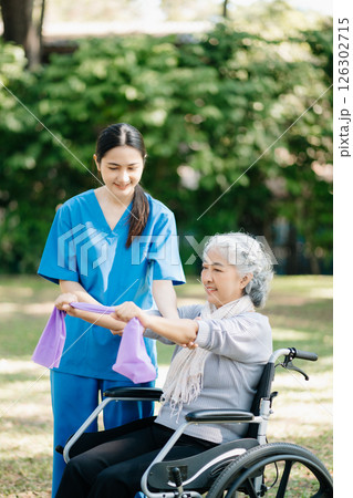 Asian physiotherapist helping elderly woman patient stretching arm during exercise correct with dumbbell in hand during training hand with patient Back problems in the garden. Asian physiotherapist helping elderly woman patient stretching arm during exercise correct with dumbbell in hand during training hand with patient Back problems in the garden. 126302715