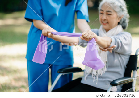 Asian physiotherapist helping elderly woman patient stretching arm during exercise correct with dumbbell in hand during training hand with patient Back problems in the garden. 126302716