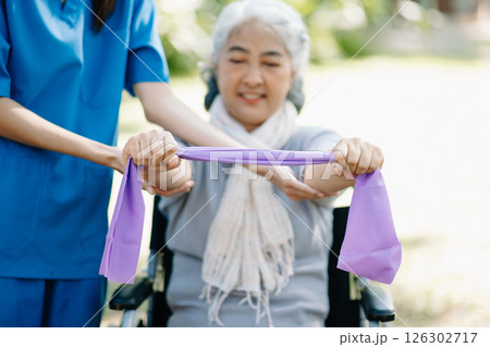 Asian physiotherapist helping elderly woman patient stretching arm during exercise correct with dumbbell in hand during training hand with patient Back problems in the garden. 126302717