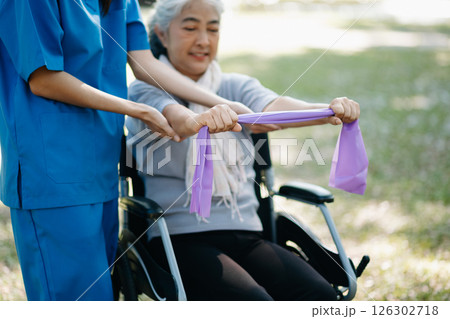 Asian physiotherapist helping elderly woman patient stretching arm during exercise correct with dumbbell in hand during training hand with patient Back problems in the garden. 126302718
