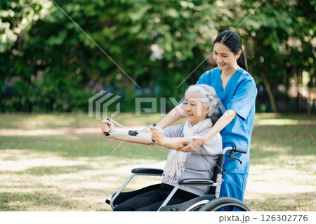 Asian physiotherapist helping elderly woman patient stretching arm during exercise correct with dumbbell in hand during training hand with patient Back problems in the garden. 126302776