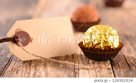 A gold wrapped chocolate praline with a gift tag on a rustic wooden table. 126302814