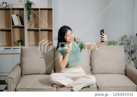 Young asian woman using smartphone and tablet while seated on couch at home Young asian woman using smartphone and tablet while seated on couch at home 126303332