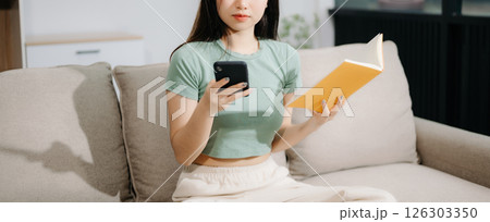 Young Asian woman listening music from headphones and writing note for her work idea in diary book. 126303350