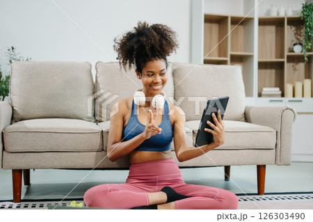 Active woman in athleisure sitting on yoga mat with tablet, headphones and modern home lifestyle. 126303490