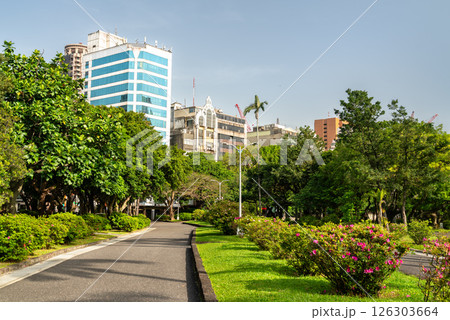 Lush garden path inside 228 Peace Memorial Park in Taipei, Taiwan, framed by blooming azaleas, manicured hedges, and dense trees with a backdrop of city buildings. This tranquil urban park 126303664