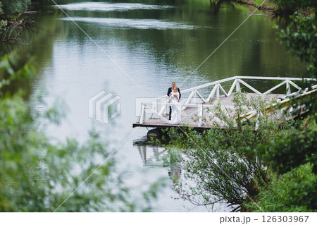 Beautiful newlywed couple in love posing on wooden pier with river in background 126303967