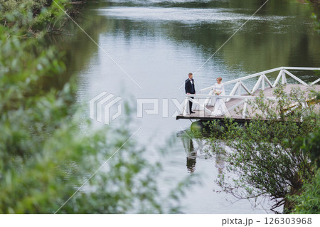 Beautiful newlywed couple in love posing on wooden pier with river in background 126303968