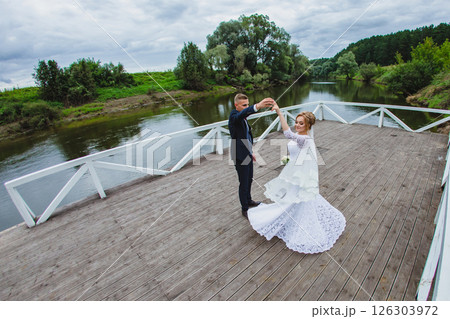 Beautiful newlywed couple in love posing on wooden pier with river in background Beautiful newlywed couple in love posing on wooden pier with river in background 126303972