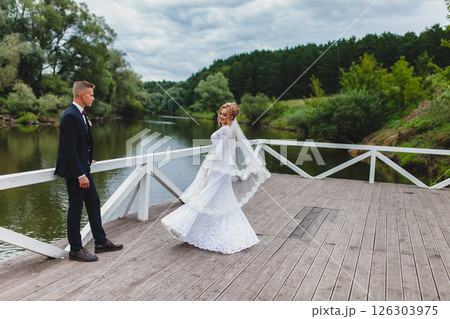 Beautiful newlywed couple in love posing on wooden pier with river in background Beautiful newlywed couple in love posing on wooden pier with river in background 126303975