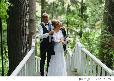 Beautiful newlywed couple in love posing on wooden stairs in summer park Beautiful newlywed couple in love posing on wooden stairs in summer park 126303979