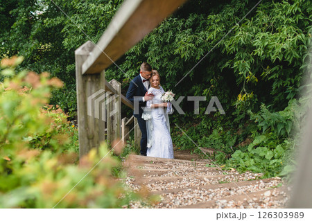 Beautiful newlywed couple in love posing on wooden stairs in summer park Beautiful newlywed couple in love posing on wooden stairs in summer park 126303989