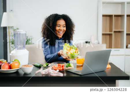 Smiling woman in a modern kitchen with fresh fruits, vegetables, blender, and orange juice, promoting clean 126304228