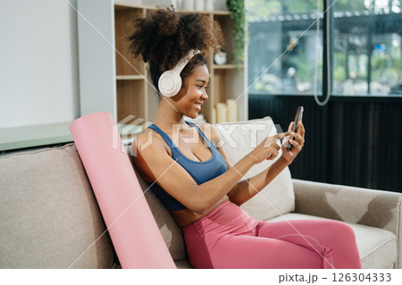 Active woman in athleisure sitting on yoga mat with tablet, headphones and modern home lifestyle. 126304333