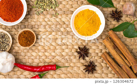A top view of various spices, herbs, and ingredients laid out on a woven mat, featuring vibrant colors and textures. A top view of various spices, herbs, and ingredients laid out on a woven mat, featuring vibrant colors and textures. 126304672