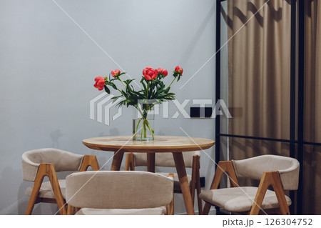 A beautiful arrangement of red peonies sits gracefully on a wooden table with accompanying chairs. A vibrant display of spring flowers in a glass vase A beautiful arrangement of red peonies sits gracefully on a wooden table with accompanying chairs. A vibrant display of spring flowers in a glass vase 126304752