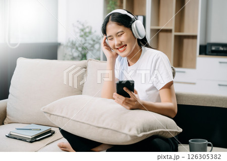 Young asian woman using smartphone and tablet while seated on couch Young asian woman using smartphone and tablet while seated on couch 126305382