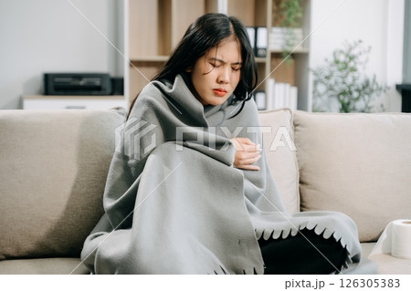 Young Asian woman suffering from flu symptoms, covered with a blanket on a sofa. Concept of illness, healthcare, Young Asian woman suffering from flu symptoms, covered with a blanket on a sofa. Concept of illness, healthcare, 126305383
