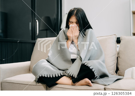 Young Asian woman suffering from flu symptoms, covered with a blanket on a sofa. Concept of illness, healthcare, 126305384