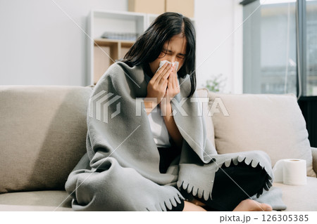 Young Asian woman suffering from flu symptoms, covered with a blanket on a sofa. Concept of illness, healthcare, Young Asian woman suffering from flu symptoms, covered with a blanket on a sofa. Concept of illness, healthcare, 126305385