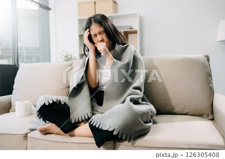 Young Asian woman suffering from flu symptoms, covered with a blanket on a sofa. Concept of illness, healthcare, 126305408