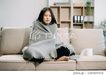 Young Asian woman suffering from flu symptoms, covered with a blanket on a sofa. Concept of illness, healthcare, 126305410