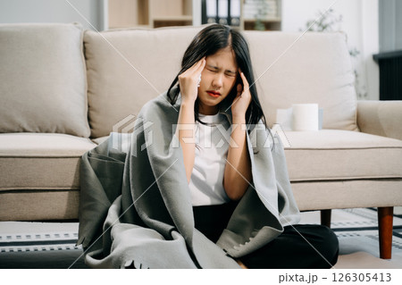 Young Asian woman suffering from flu symptoms, covered with a blanket on a sofa. Concept of illness, healthcare, 126305413