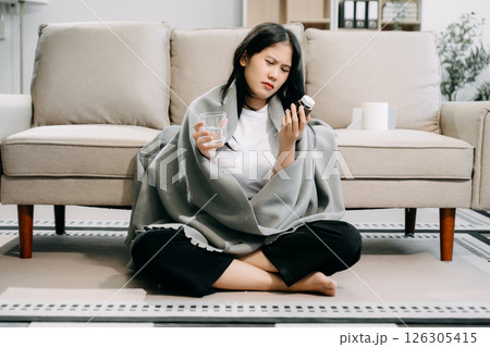Young Asian woman suffering from flu symptoms, covered with a blanket on a sofa. Concept of illness, healthcare, 126305415