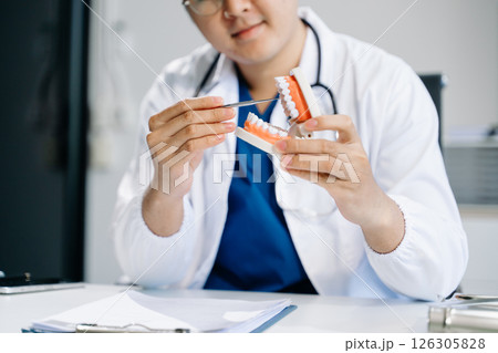 Dentist sitting at table with jaw samples tooth model and working with tablet and laptop in dental Dentist sitting at table with jaw samples tooth model and working with tablet and laptop in dental 126305828
