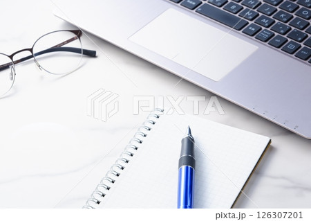 ノートにメモをとりながらノートパソコンでデスクワークをしているイメージ ノートにメモをとりながらノートパソコンでデスクワークをしているイメージ 126307201