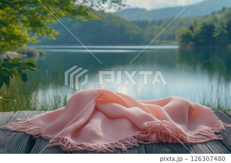 A pink blanket with fringes lies gently on a rustic wooden dock beside a calm forest lake A pink blanket with fringes lies gently on a rustic wooden dock beside a calm forest lake 126307480