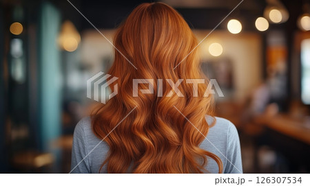 Glossy red waves falling down a back, lit by soft warm light in a warmly decorated indoor space 126307534