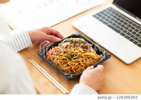 会社のデスクで焼きそばお好み焼きランチを食べるミドル女性 126308303